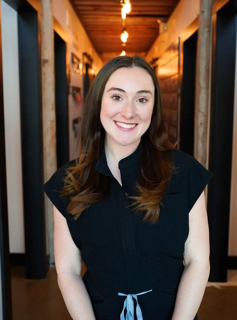Smiling woman in black uniform standing in a warmly lit hallway
