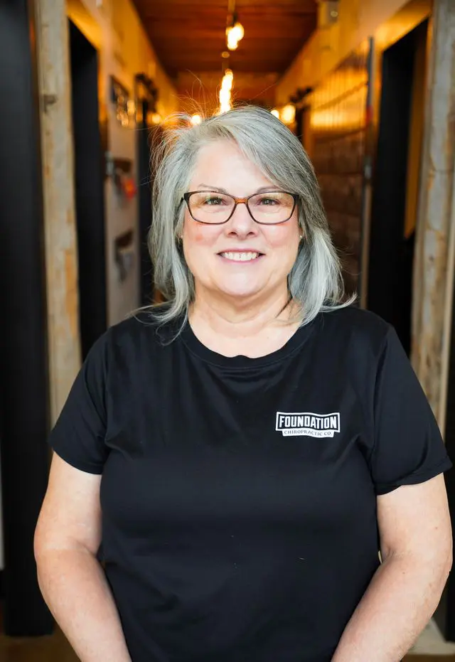 Smiling woman with gray hair and glasses wearing a black shirt