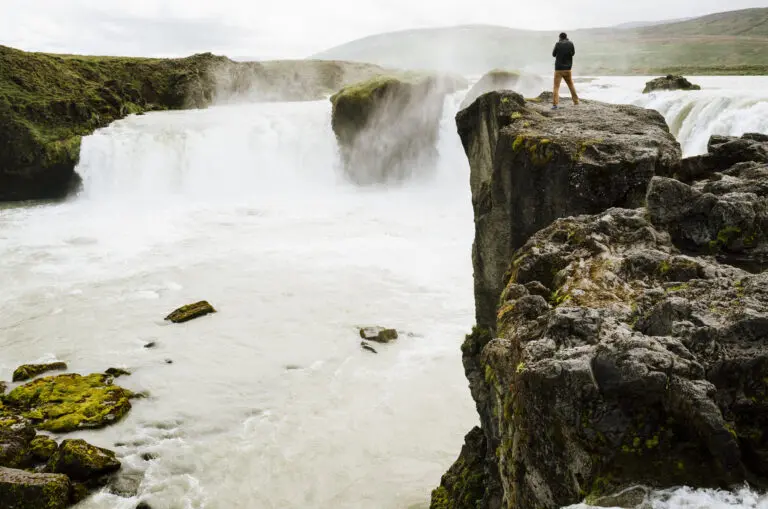 Person standing near a stream by a cliff overlooking a river
