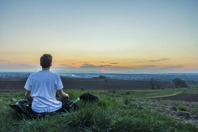 Person sitting cross-legged meditating outdoors during sunset