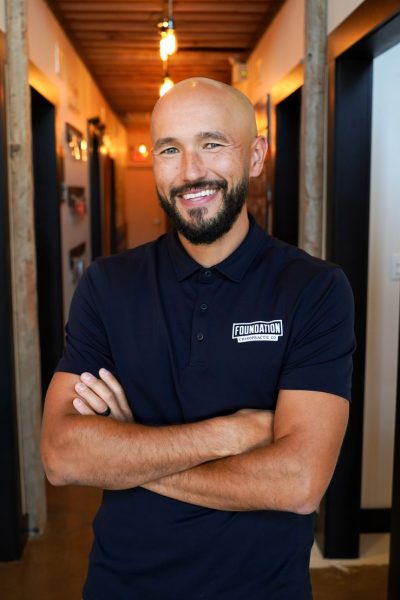 Smiling chiropractor standing with arms crossed in a clinic hallway